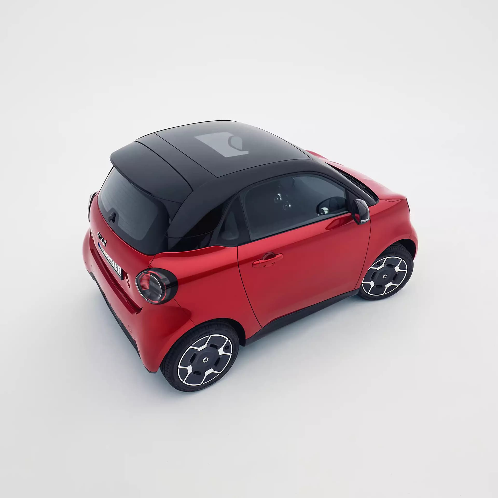 Roter smart #2 mit schwarzem Panoramadach und markanten Leichtmetallfelgen aus erhöhter Heck- und Seitenperspektive vor weißem Hintergrund.