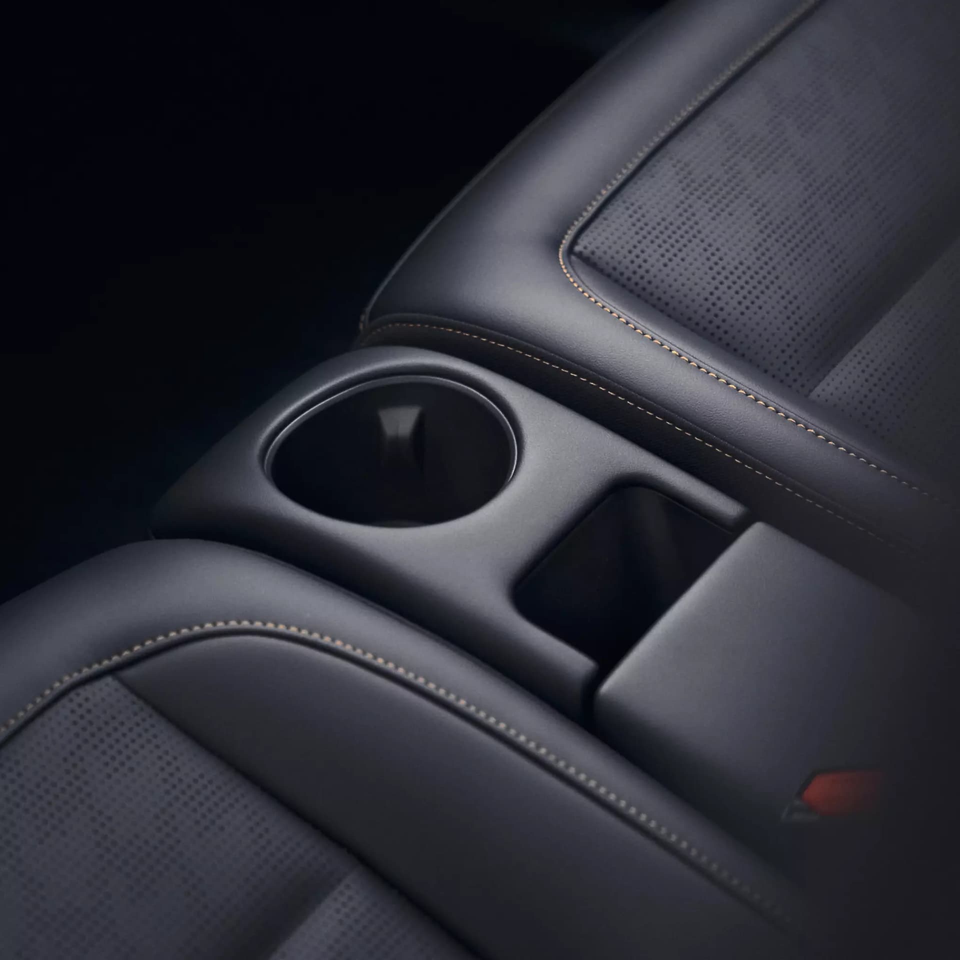 Detailaufnahme des smart #2 Innenraums mit schwarzen, perforierten Sitzen, Kontrastnähten sowie integriertem Getränkehalter und Ablagefach zwischen den Sitzen.