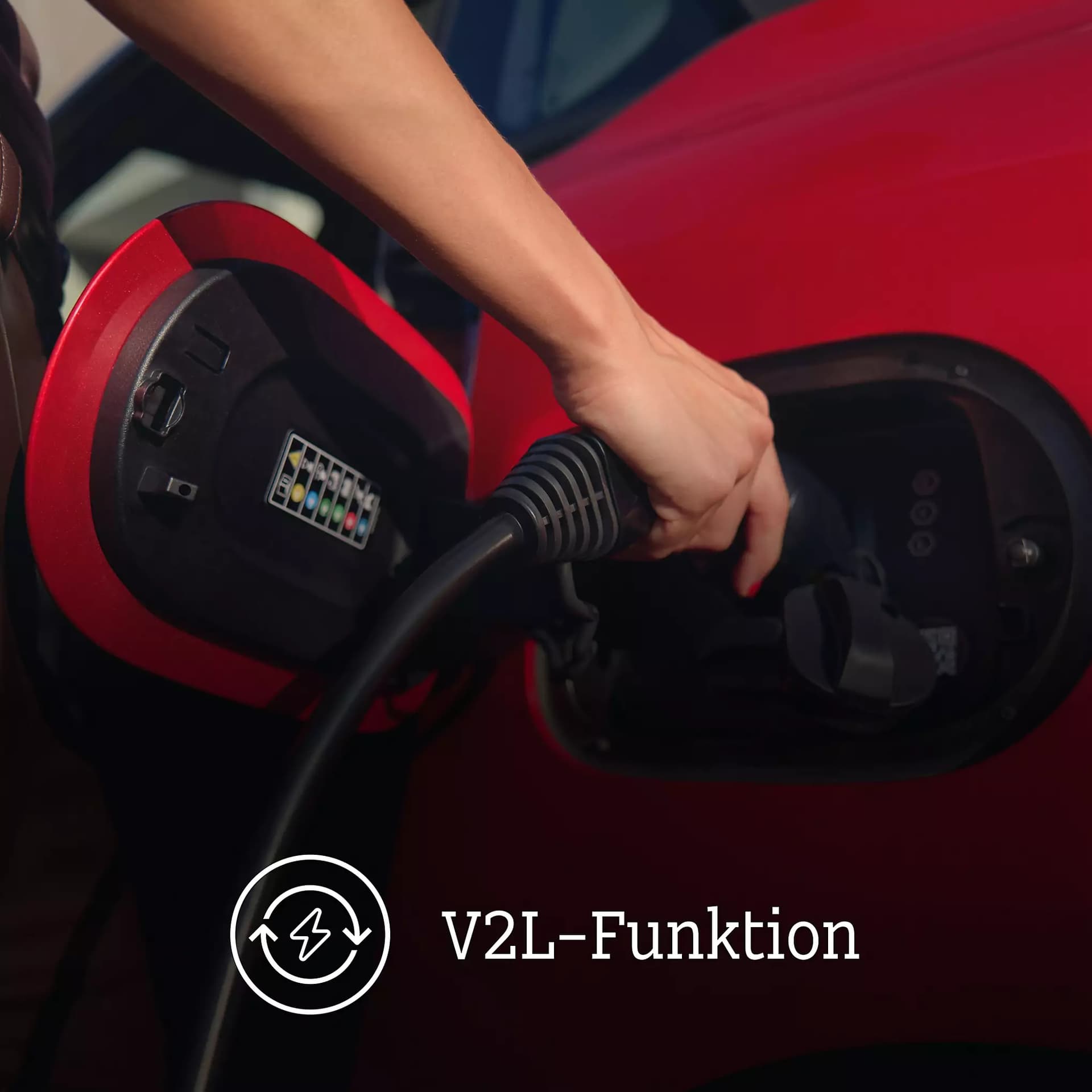 Detailaufnahme des Ladeanschlusses eines roten smart #2 mit Ladestecker und dem Hinweis auf die Vehicle-to-Load-Funktion (V2L).