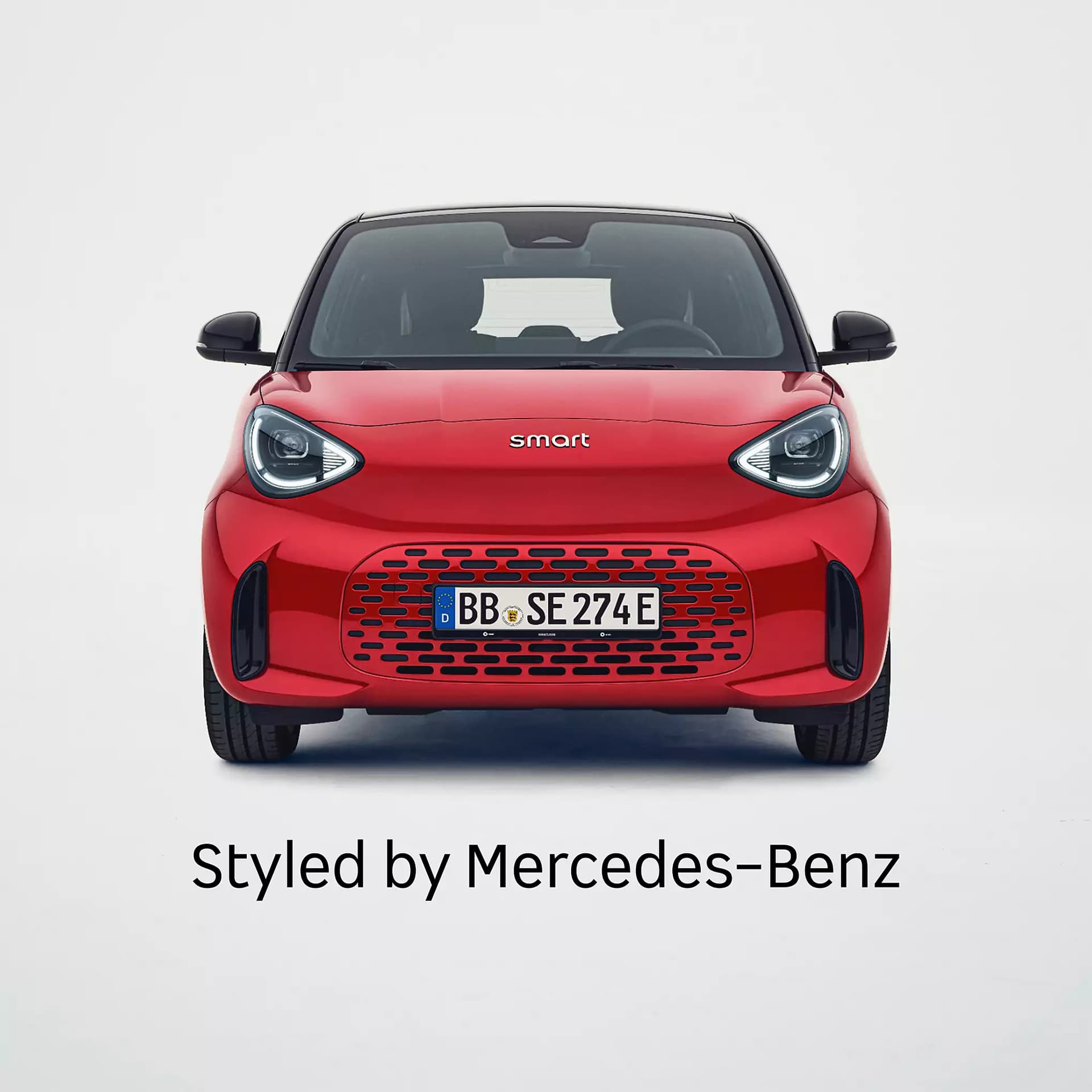 Frontansicht eines roten smart #2 mit schwarzem Dach, markanten LED-Scheinwerfern und dem Schriftzug „Styled by Mercedes-Benz“ vor weißem Hintergrund.