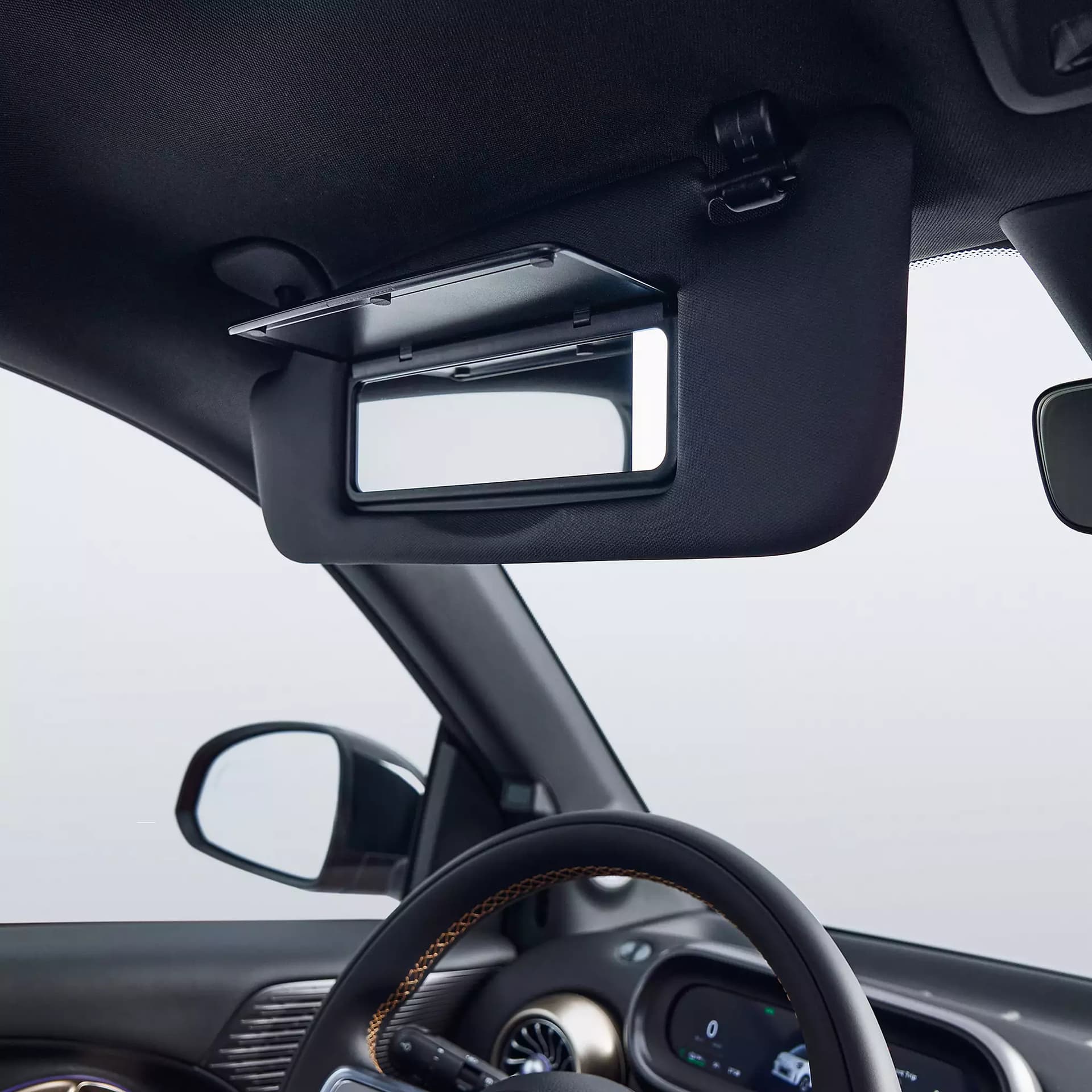 Detailaufnahme der heruntergeklappten Sonnenblende mit geöffnetem Kosmetikspiegel im smart #2, darunter das Lenkrad und Teile des Cockpits.