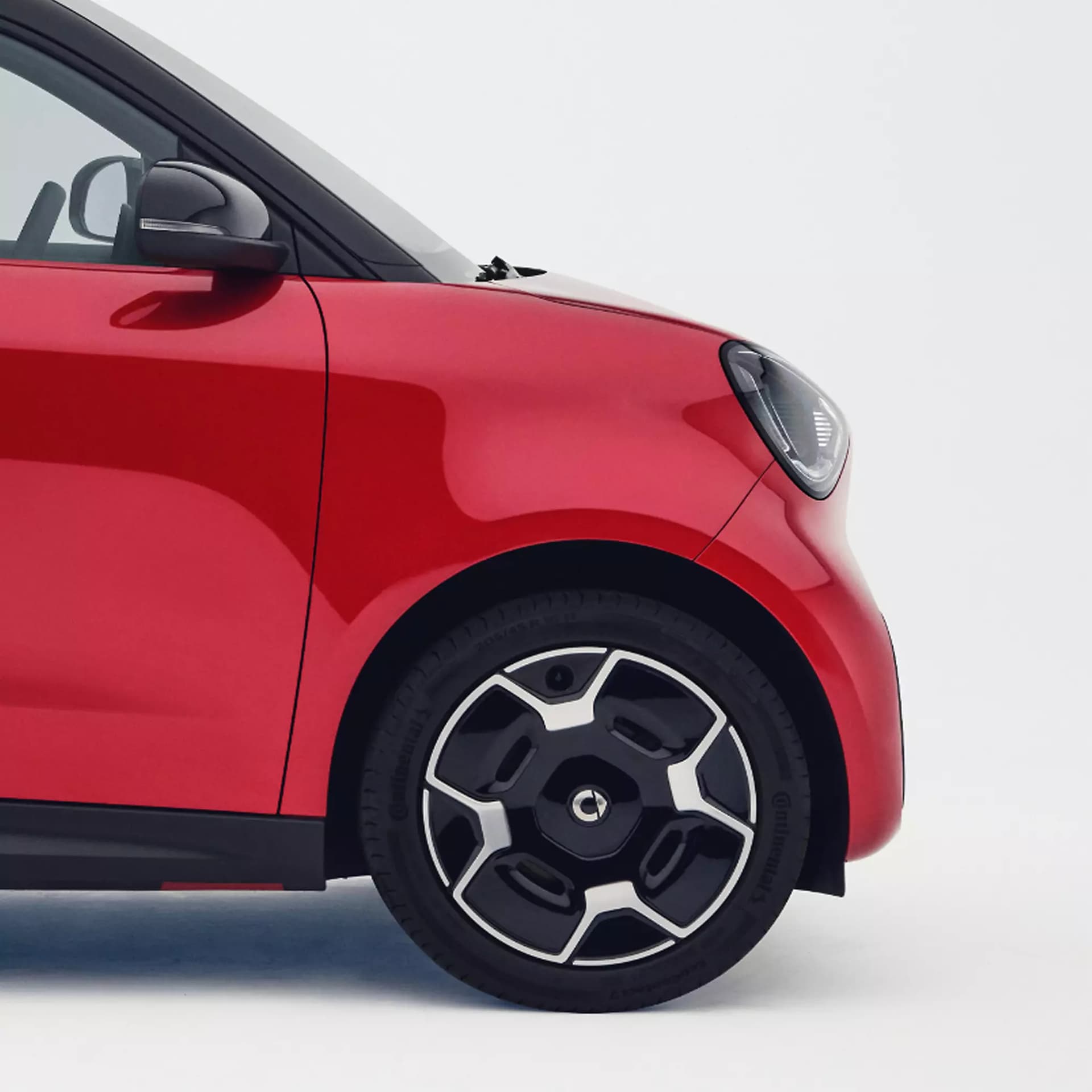 Detailaufnahme der roten Karosserie des smart #2 mit markanter 16-Zoll-Leichtmetallfelge, schwarzem Außenspiegel und LED-Scheinwerfer.